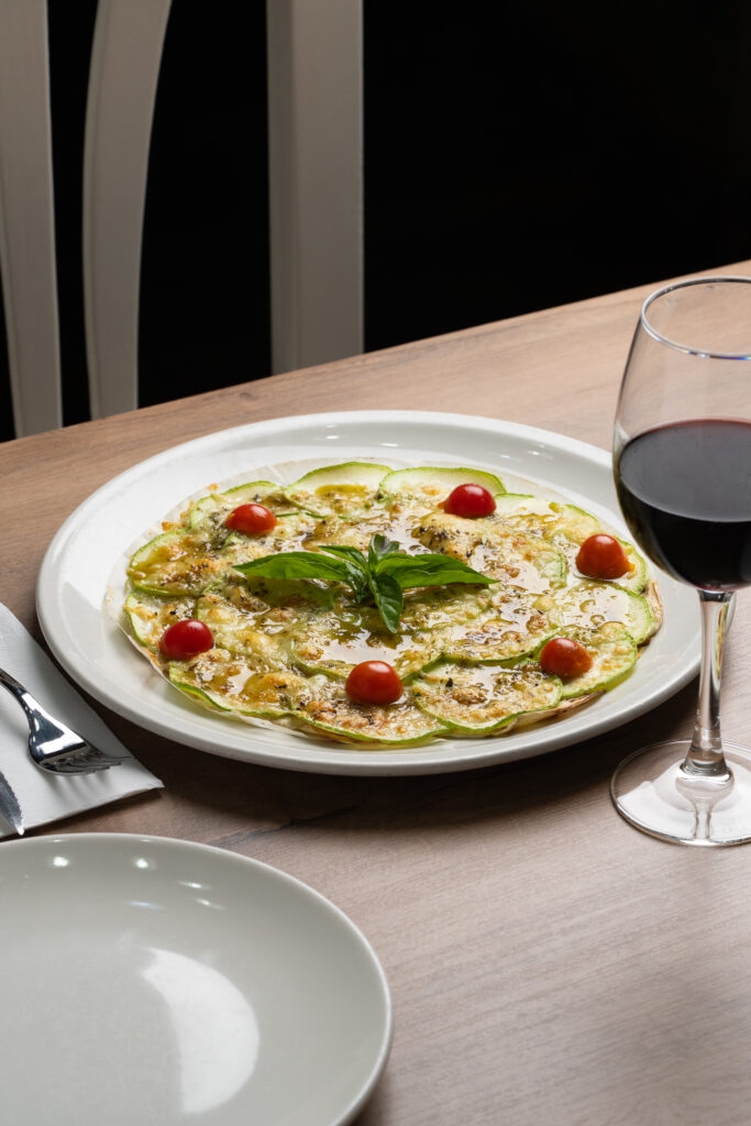 Plato de carpaccio de Pizzería Vesubio servido junto a una copa de vino tinto